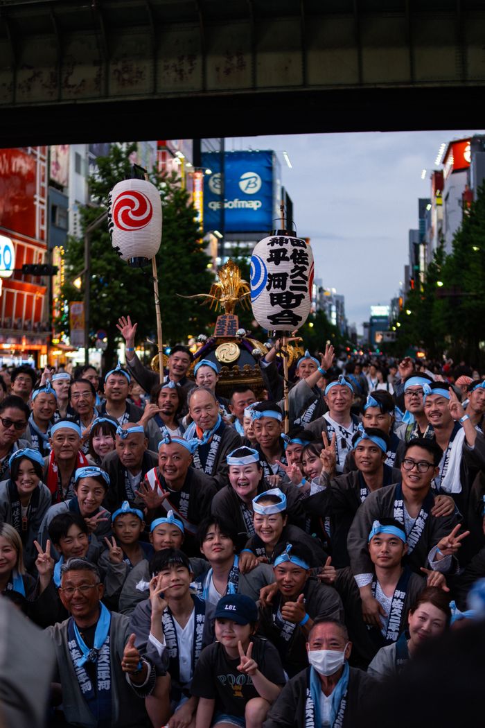 Large group celebrating during a vibrant Japanese festival under a city bridge.
