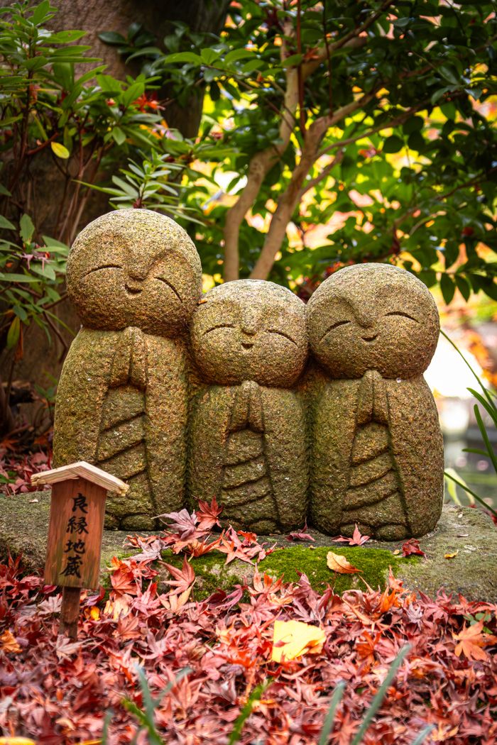 Three Jizo statues surrounded by autumn leaves in Kamakura, Japan garden.